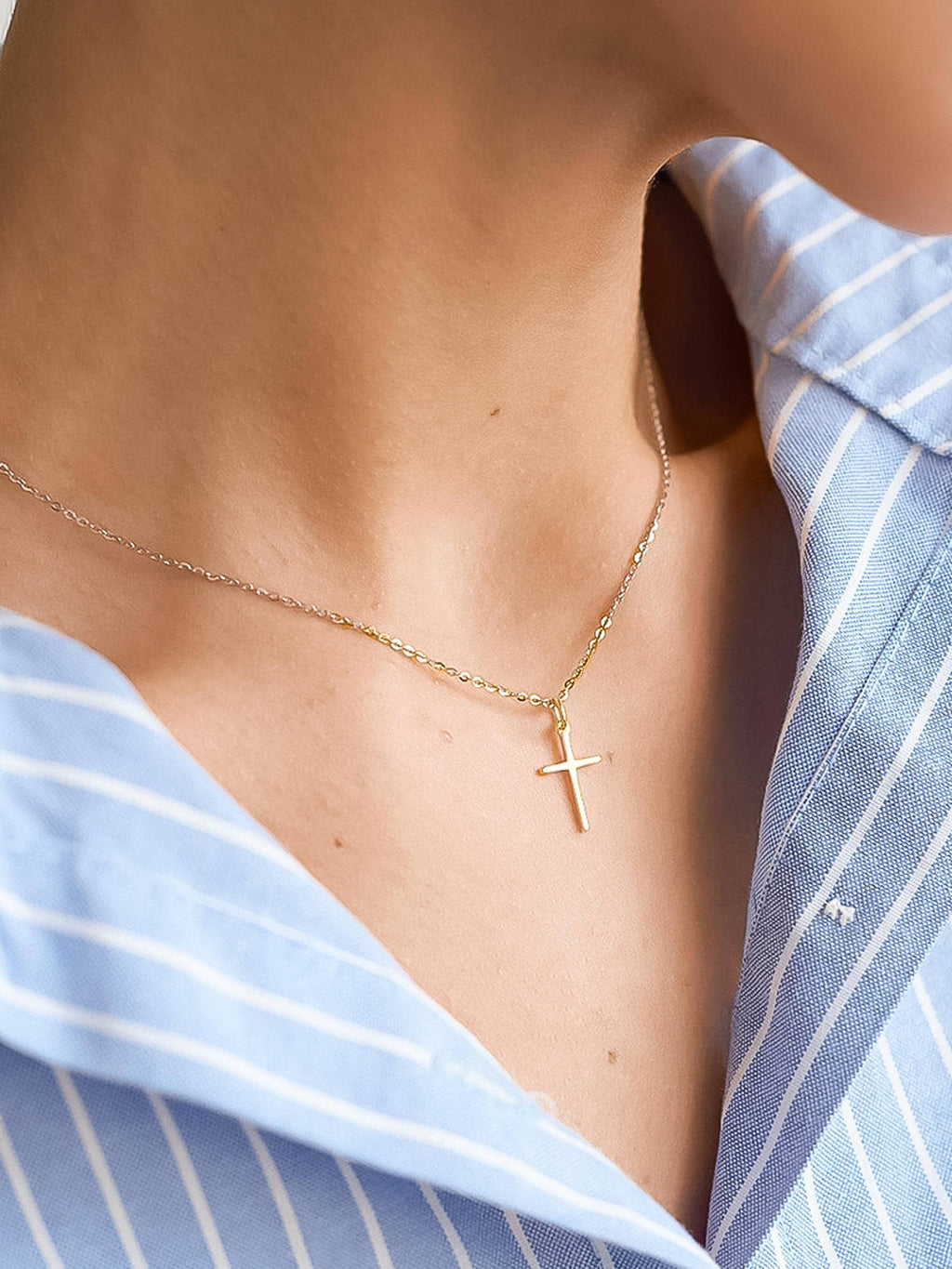 Gold necklace with a cross pendant worn by a person in a blue striped shirt.