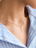 Gold necklace with a cross pendant worn by a person in a blue striped shirt.